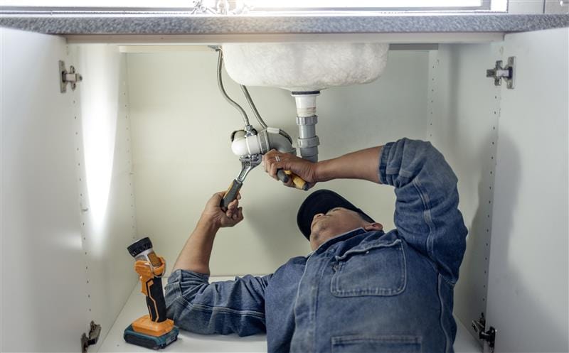 Plumber repairing pipes beneath a bathroom sink in Fountain Valley